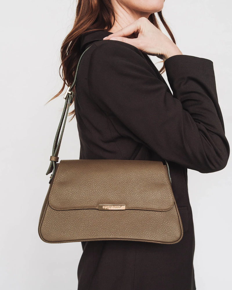 Pebbled leather flap shoulder bag with gold logo, worn by woman in blazer. The High Line Shoulder Bag Tapenade.