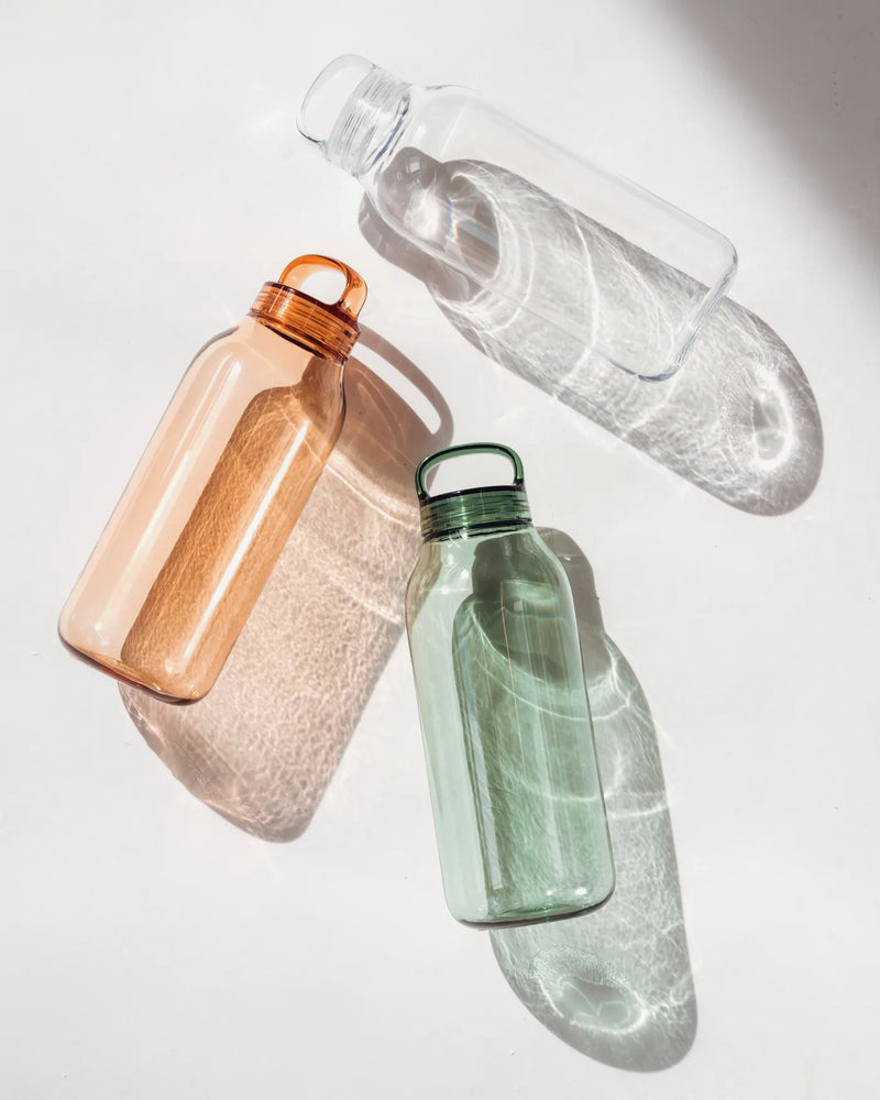 Three Kinto water bottles in amber, clear, and sage displayed on a white surface. The Kinto Water Bottle Clear.