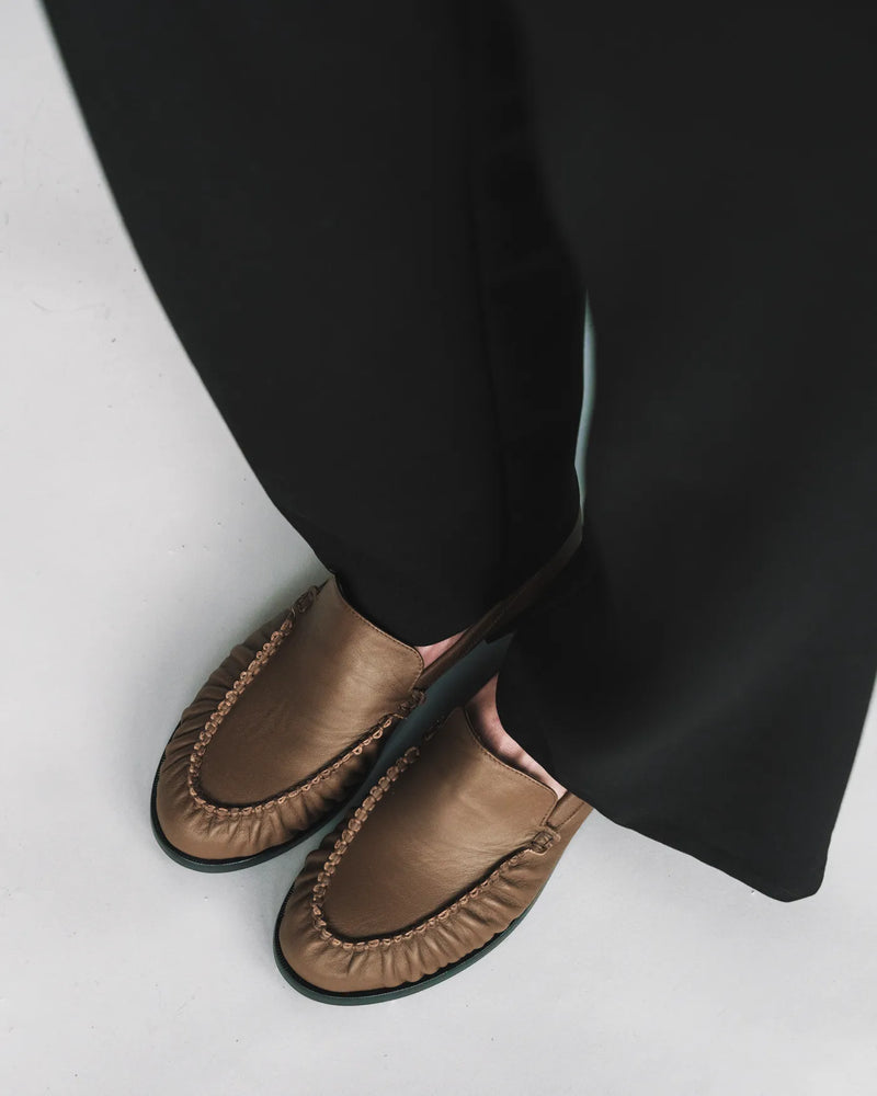 Leather loafers with ruched toe, styled with black wide-leg trousers. The Laid Back Loafer Tapenade. Sizes 5–12.