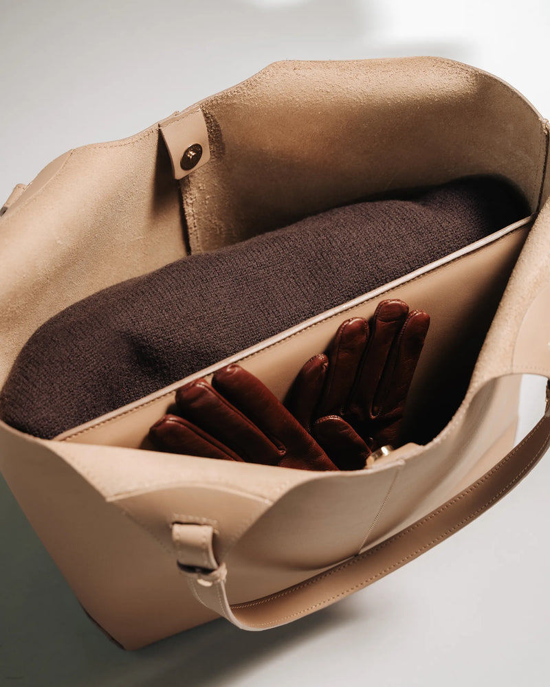 Interior view of a leather tote open, with a knit sweater and brown leather gloves inside. The Lisboa Tote Biscotti.