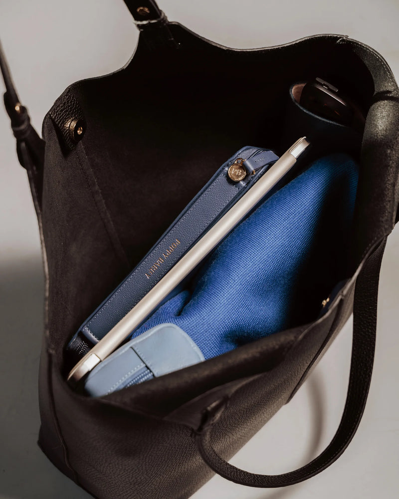 Interior view of pebbled leather tote with laptop, navy case, blue sweater, and bottle inside. The Lisboa Tote Black.