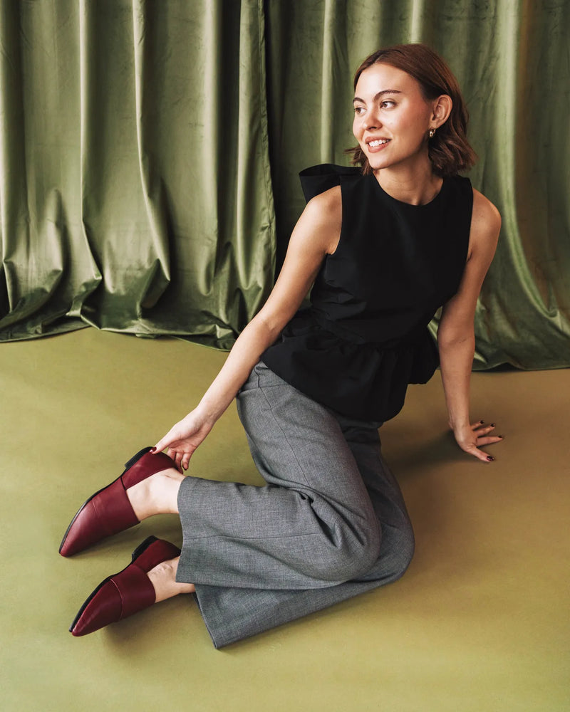 Woman seated on floor wearing resort red pointed-toe flats with grey trousers. The Luxe Fit Flat Resort Red. Sizes 5–12.