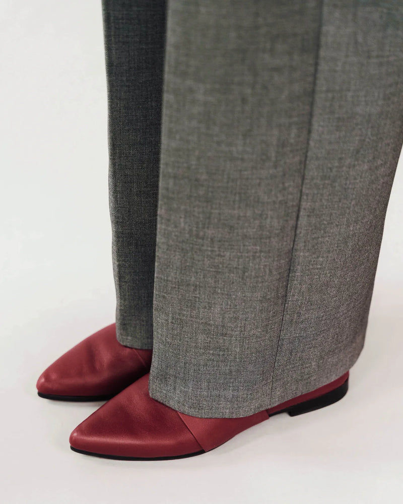 Close-up of resort red pointed-toe leather flats worn with grey wide-leg trousers. The Luxe Fit Flat Resort Red. Sizes 5–12.