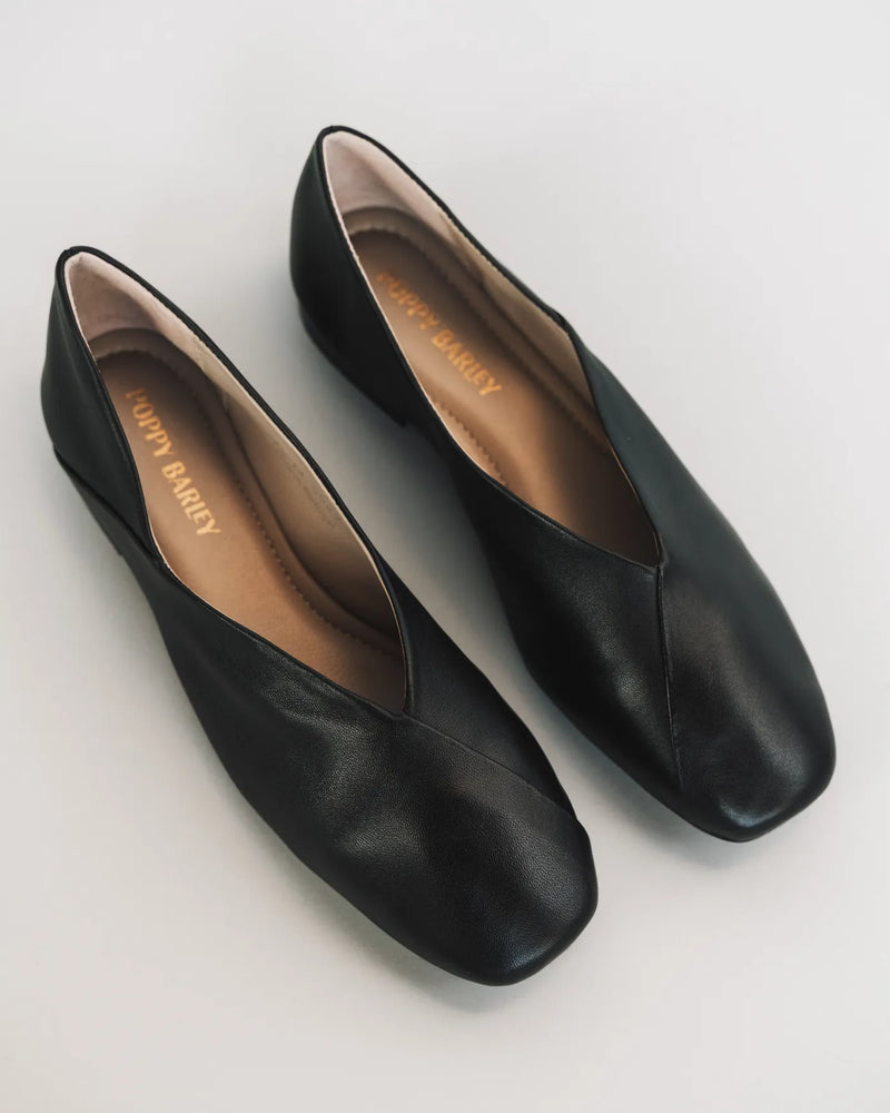 Leather square-toe flats on white, insoles visible. The Marché Flat Black. Sizes 5–12, available in wide.