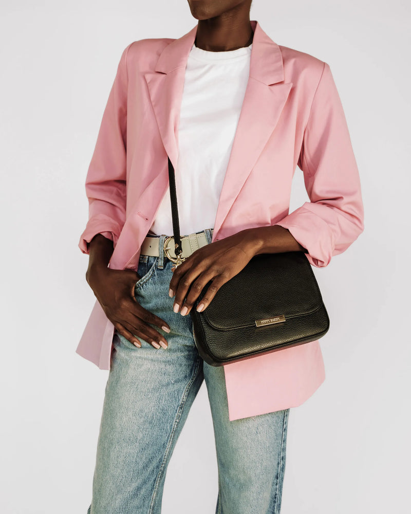 Woman in pink blazer and jeans wearing a pebbled leather crossbody bag. The Medium Day to Night Bag Black Pebble.