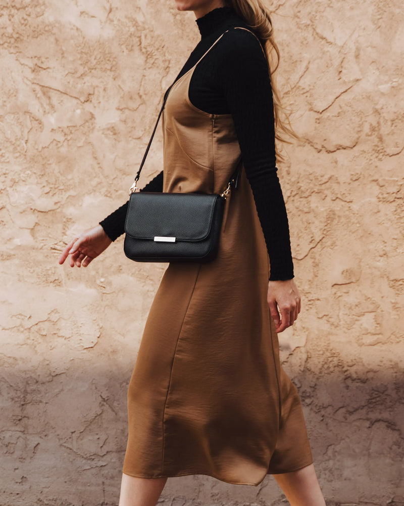 Woman in camel slip dress, black turtleneck, pebbled leather crossbody. The Medium Day to Night Bag Black Pebble.