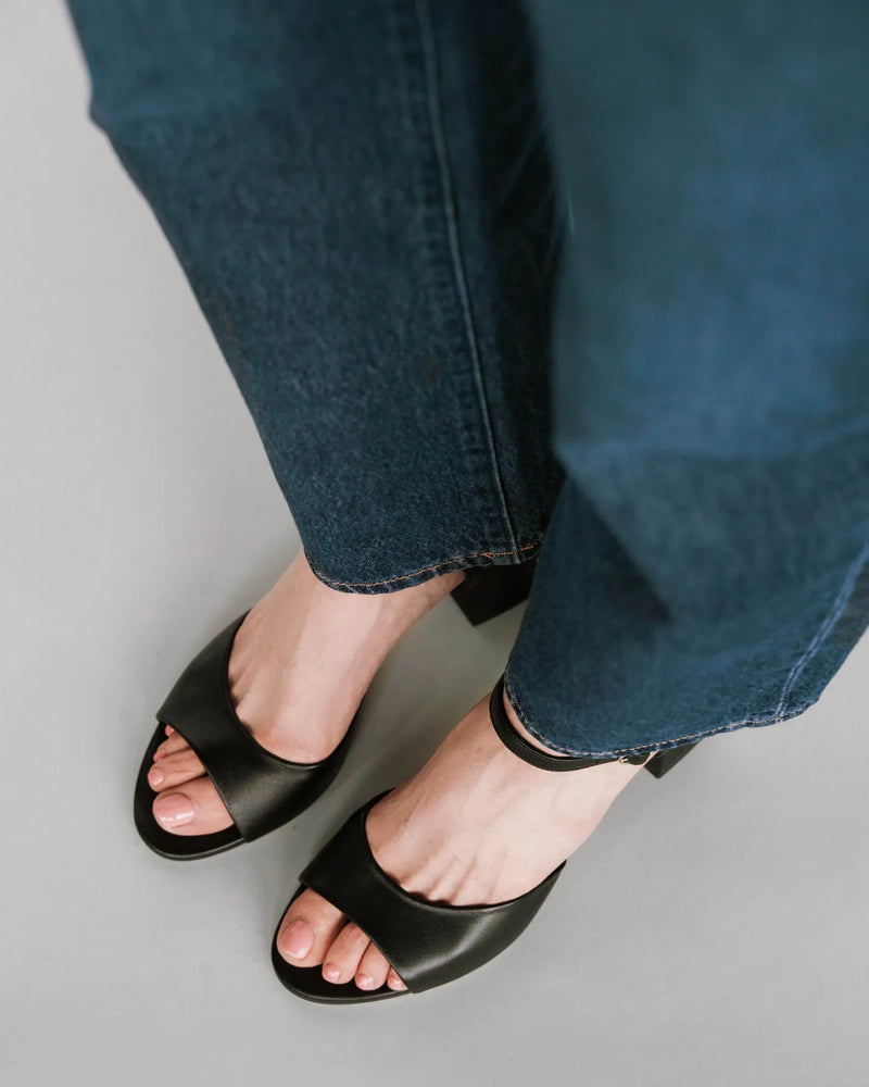 Leather block-heeled sandals with ankle strap, overhead view with dark jeans. The Mila Heeled Sandal Black. Sizes 5–12.
