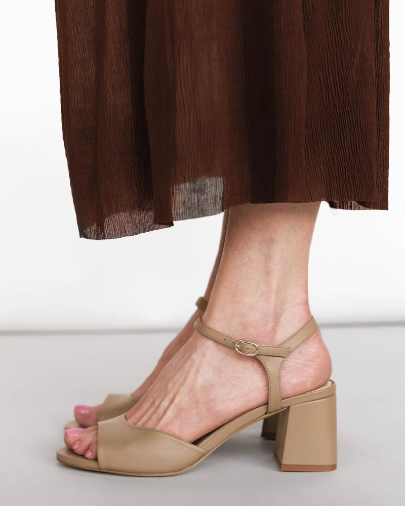 Leather heeled sandals with ankle strap, side view with burgundy skirt. The Mila Heeled Sandal Halva. Sizes 5–12.