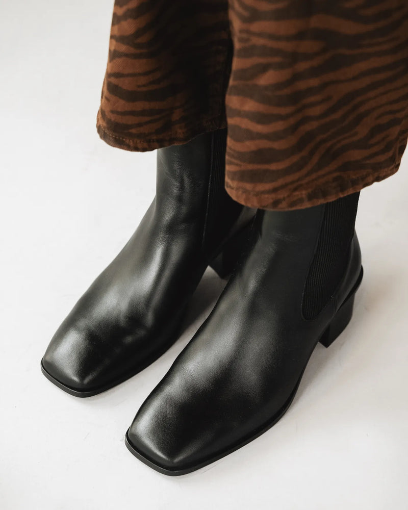 Woman in tiger-print pants wears leather chelsea boots with square toe. The Quinn Chelsea Boot Black. Sizes 5–12.
