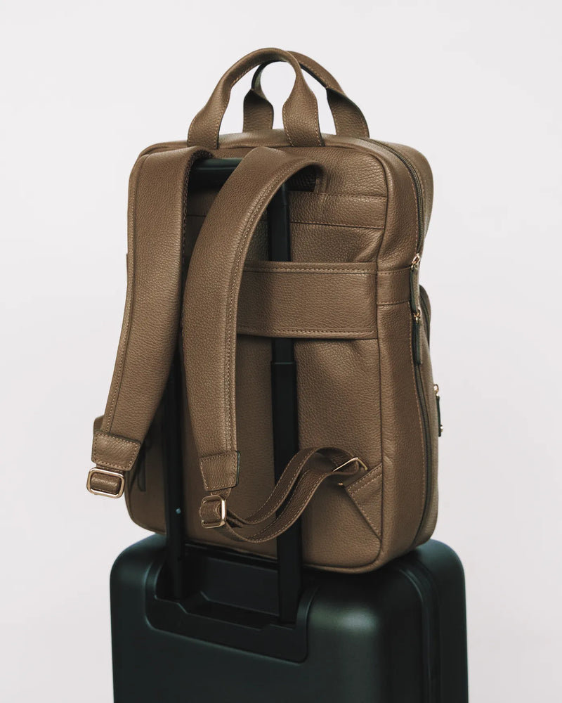 Pebbled leather backpack worn by smiling woman in black blazer. The Refined Backpack Tapenade.