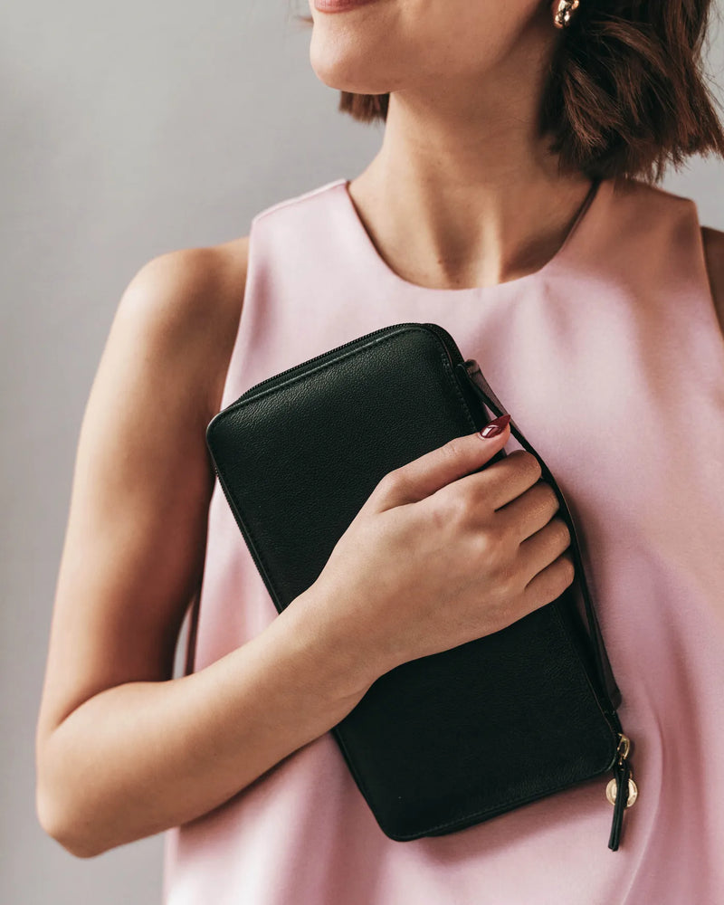 The Six Person Family Passport Holder Black Micro Pebble in leather, held by woman in pink sleeveless top