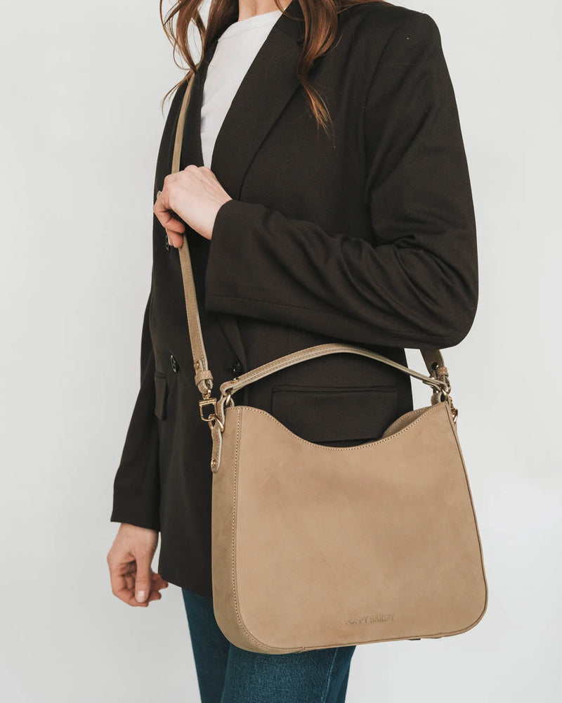 Nubuck hobo tote with crossbody strap worn by woman in black blazer and jeans. The Sixteenth Tote Clay.