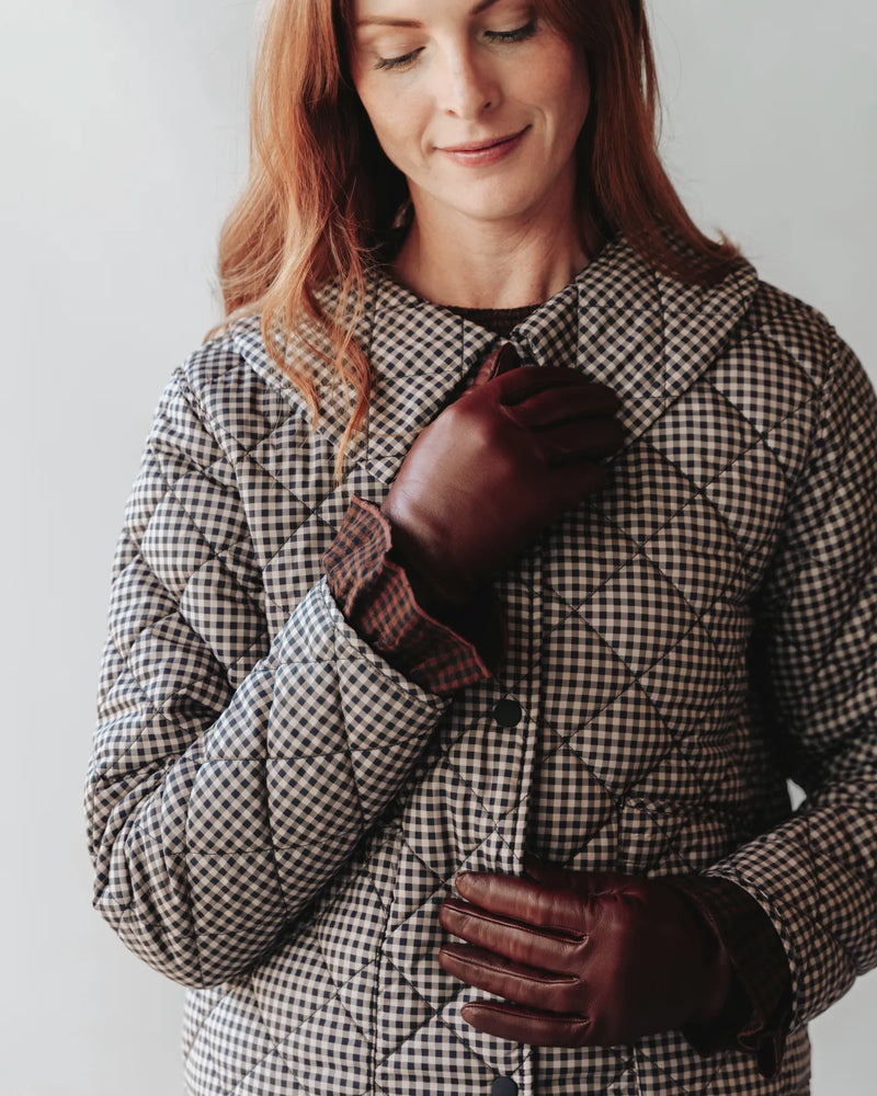Woman in houndstooth coat putting on leather gloves with ruched wrist detail. The Sleek Leather Glove Chocolate.