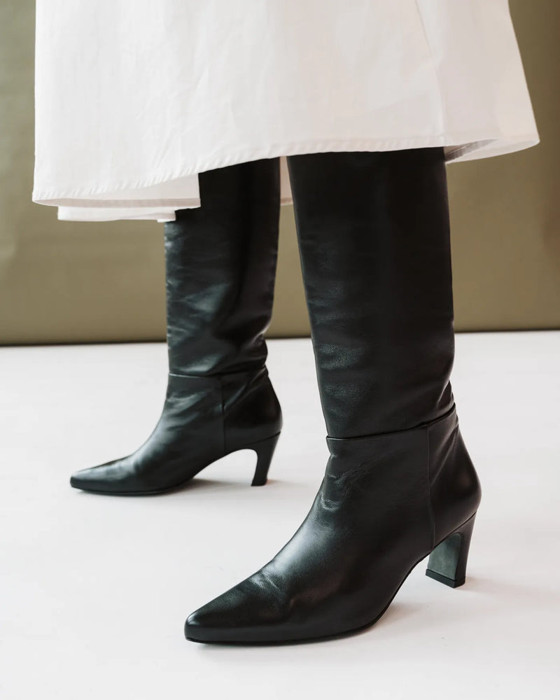 Leather tall boots on woman leggings and white skirt. The Toujours Tall Boot Black. Sizes 5–12.