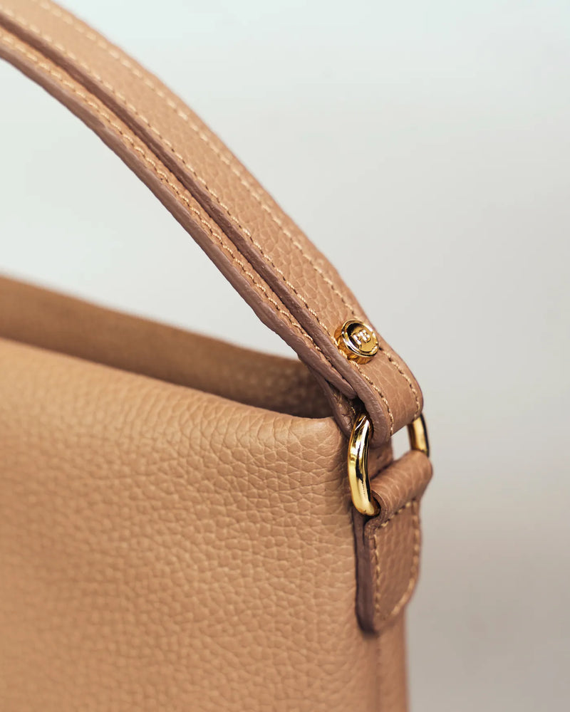 Close-up of the top handle and gold hardware on a pebbled leather mini bag. The Via Monte Bag Biscotti.