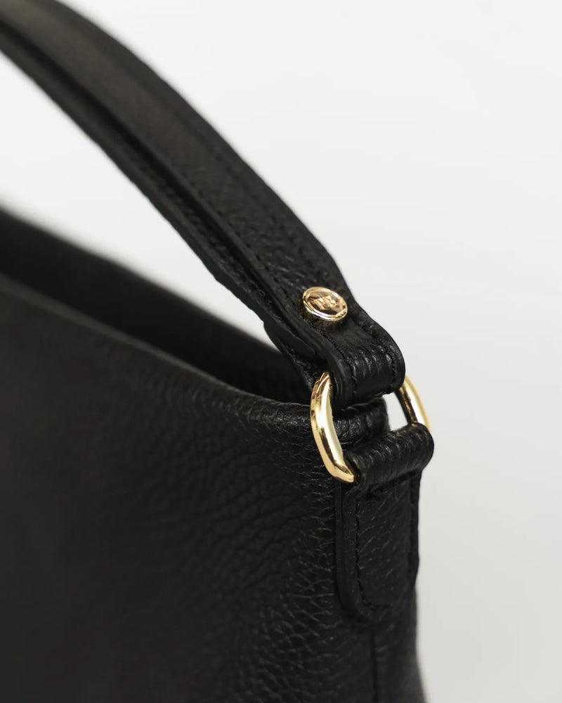 Close-up of the top handle and gold hardware on a pebbled leather mini bag. The Via Monte Bag Black.