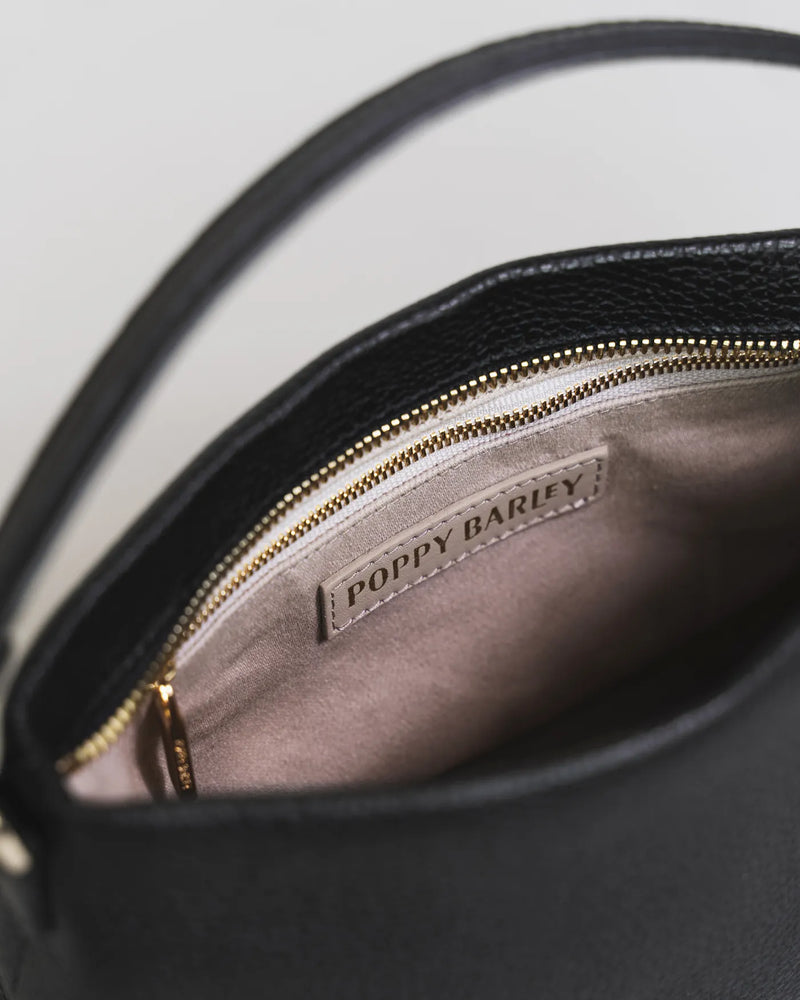Open interior of the pebbled leather mini bag with Poppy Barley branding and gold zipper. The Via Monte Bag Black.