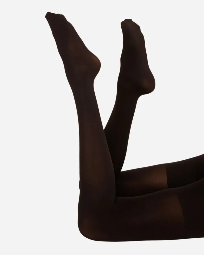 Woman lying with legs raised wearing opaque black tights. Threads Opaque Contour Black Tights.