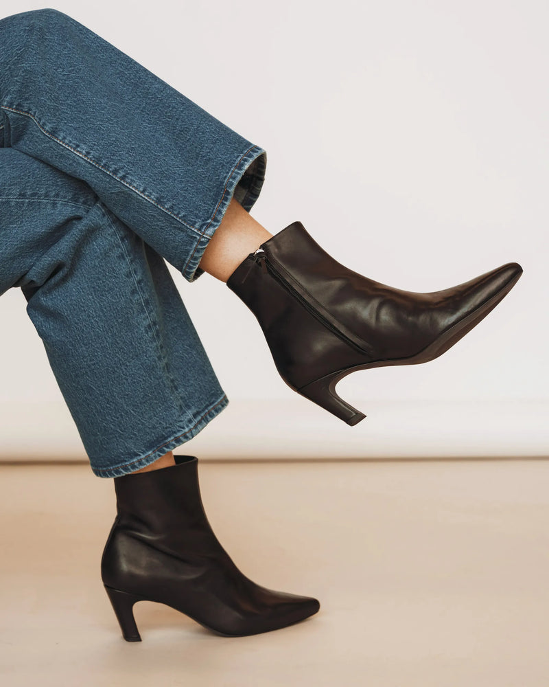 Woman in wide-leg jeans wearing The Toujours Boot Black, pointed-toe kitten heel. Sizes 5–12, wide available.