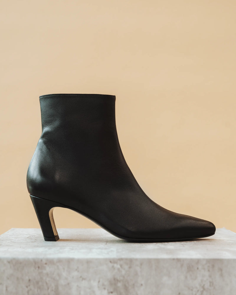 The Toujours Boot Black on marble block, side profile against warm beige background. Sizes 5–12, wide available.