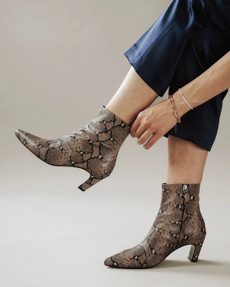 Woman in blue pants adjusting taupe snake print ankle boot. The Toujours Boot Taupe Snake. Sizes 5–12, available in wide.