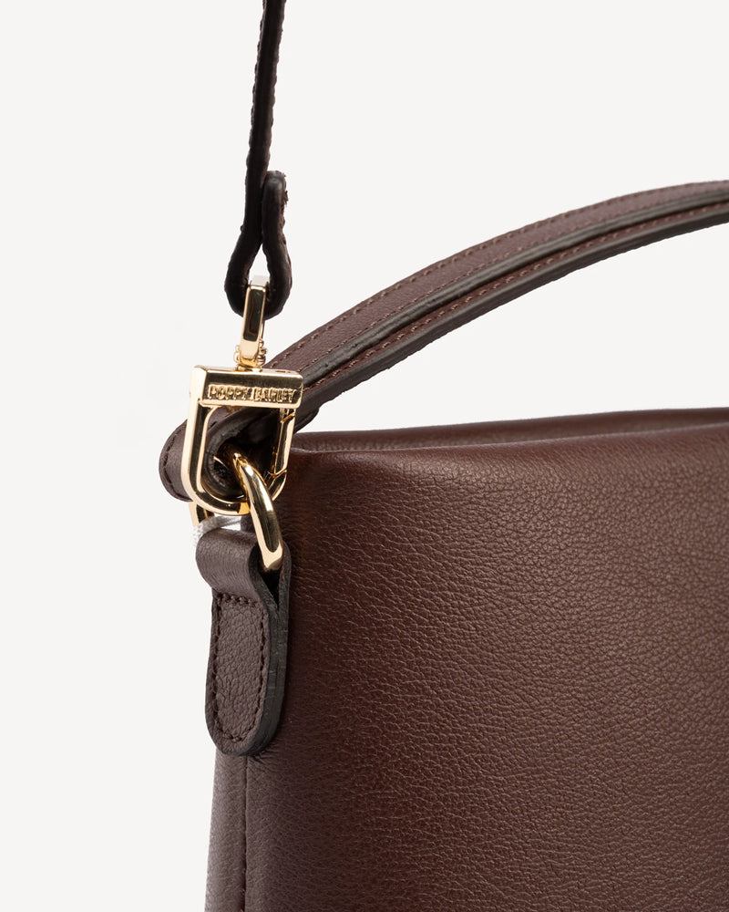 Close-up of gold-tone hardware and buckle strap detail. The Via Monte Bag French Press.