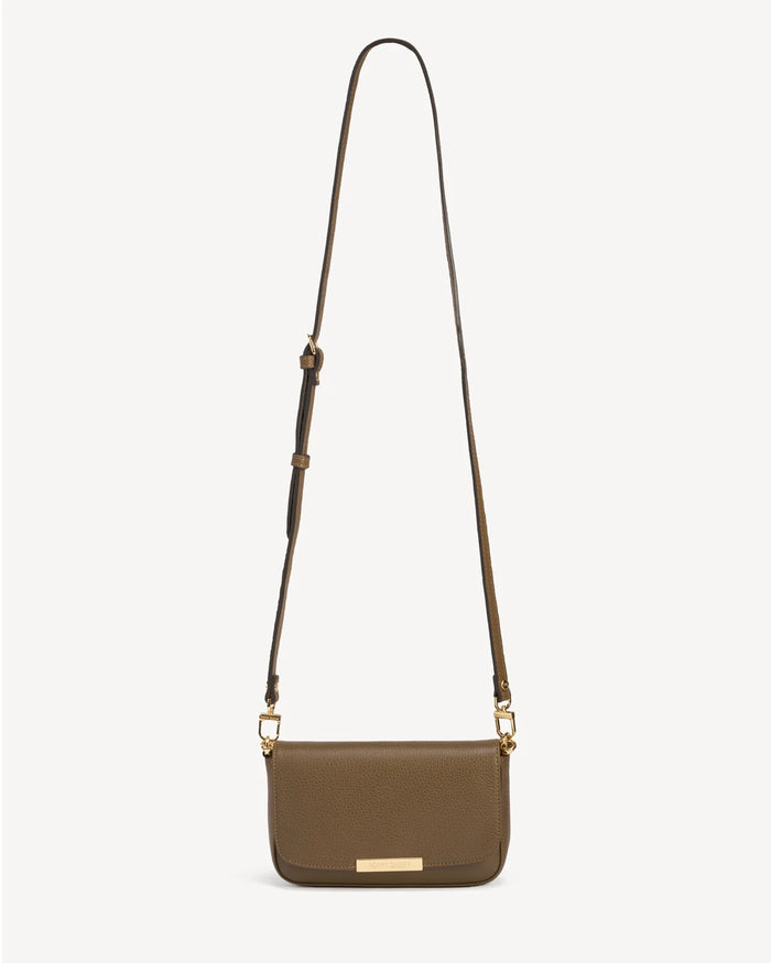 Front view of the leather flap bag with a long adjustable strap laid flat. The Day To Night Bag Tapenade.