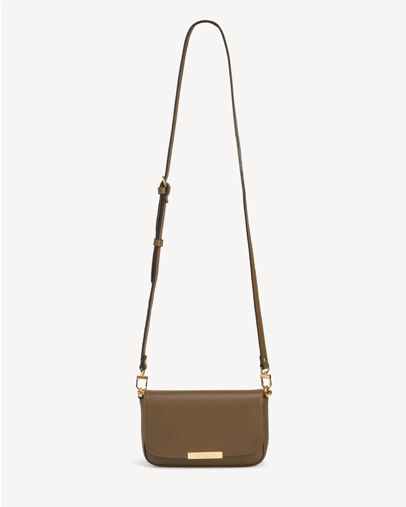 Front view of the leather flap bag with a long adjustable strap laid flat. The Day To Night Bag Tapenade.