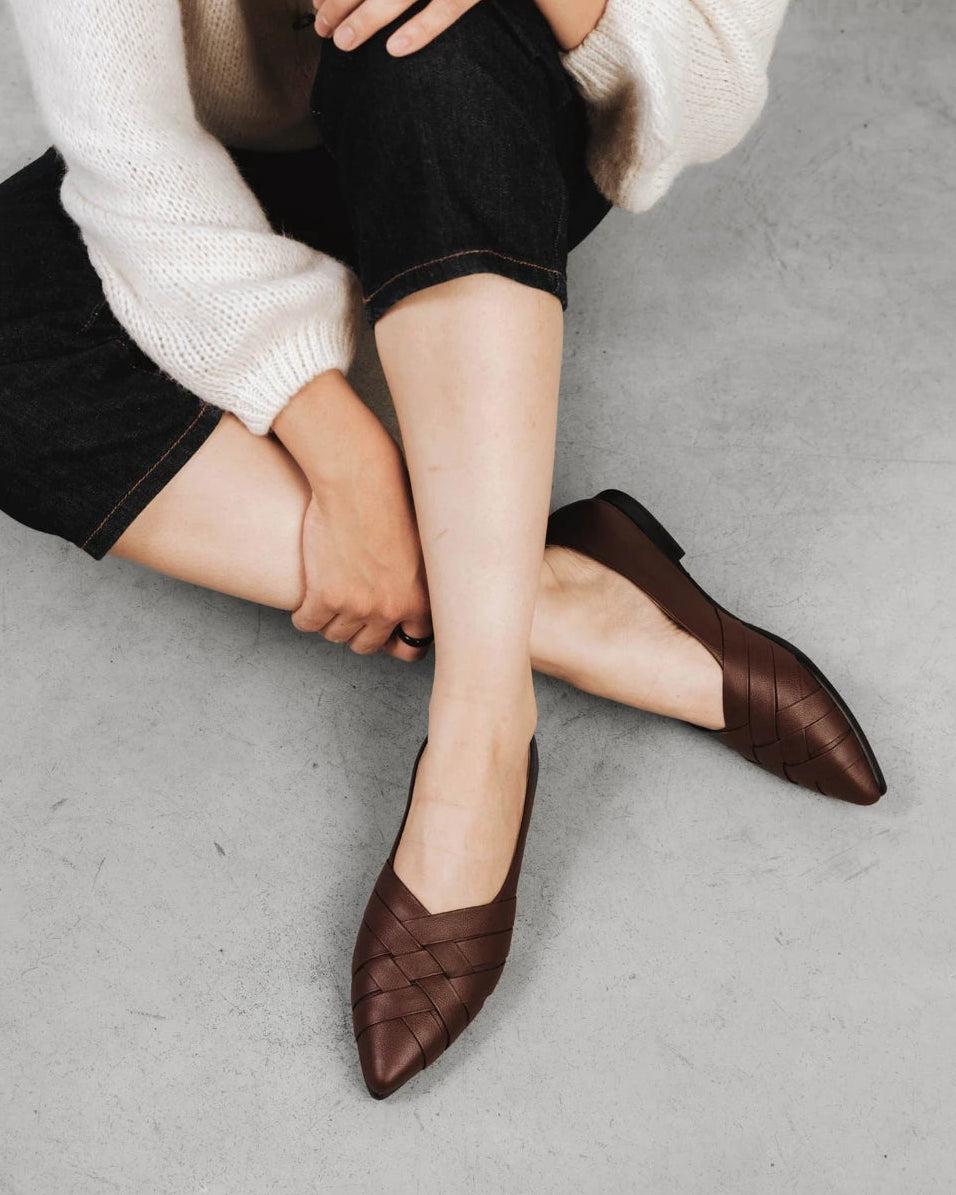 Person seated wearing woven leather flats with cropped trousers. The Athena Flat French Press. Sizes 5–12, wide available.