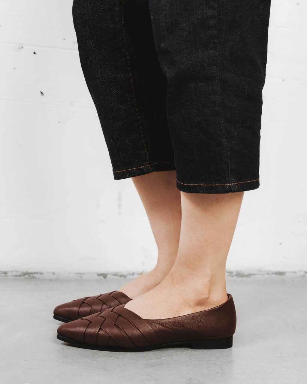 Close-up of a woven leather flat worn with cropped trousers. The Athena Flat French Press. Sizes 5–12, wide available.