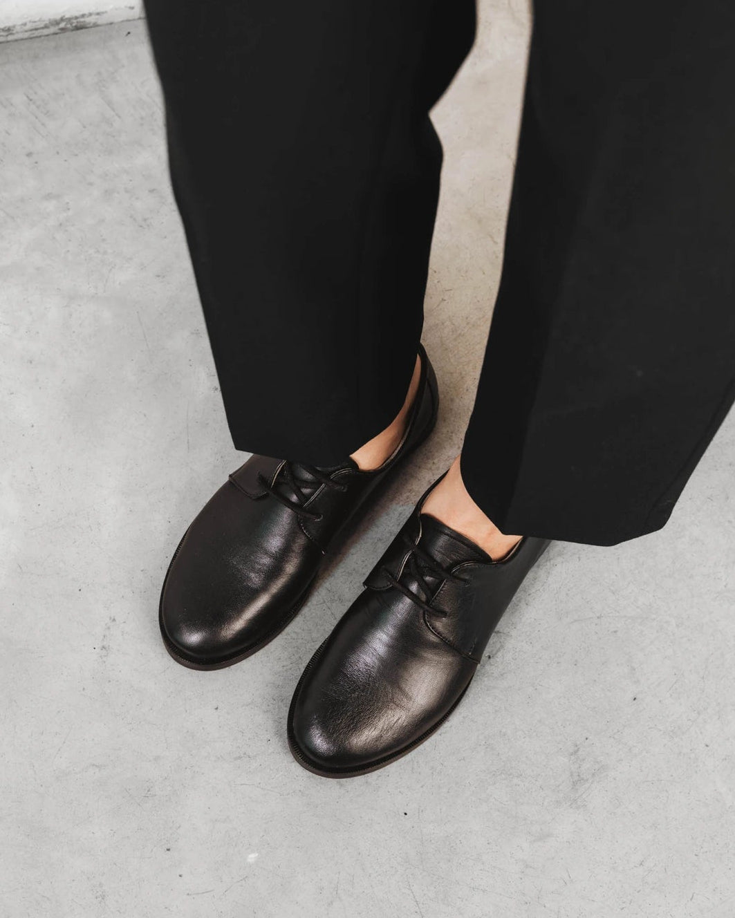 Model wearing the oxfords with tailored black trousers. The Capsule Oxford Black. Sizes 5–12, wide available.