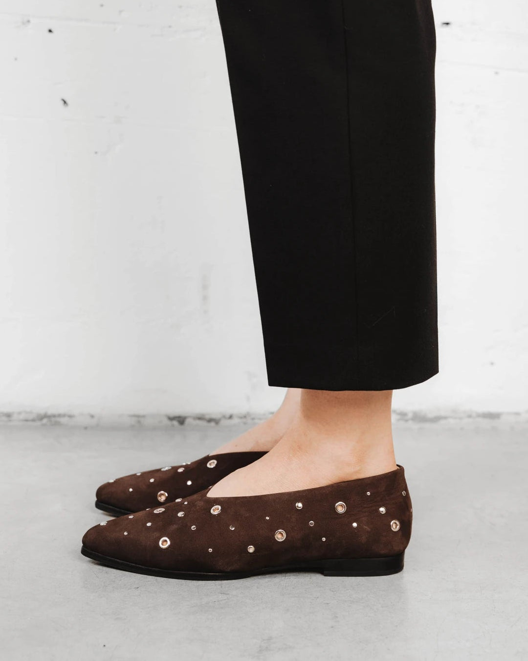 Model walking in the studded suede flats. The Atelier Flat Cocoa Plum Studded. Sizes 5–12, wide available.