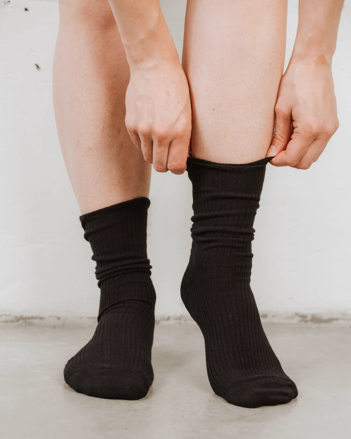 Close-up of hands pulling up the ribbed cuff. The Ribbed Crew Sock Black 3-Pack.