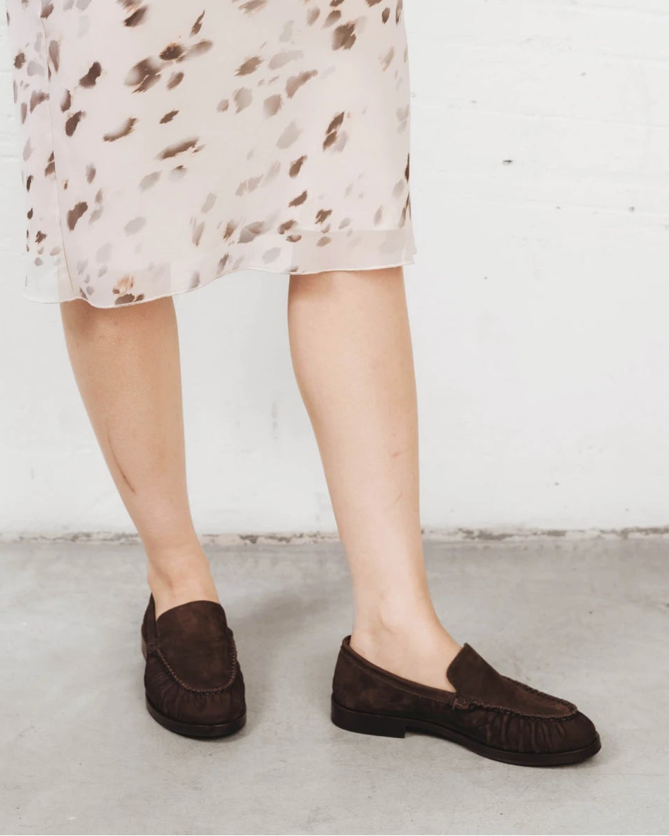 Person walking wearing suede loafers with a printed dress. The Laid Back Loafer Cocoa Plum. Sizes 5–12, wide available.