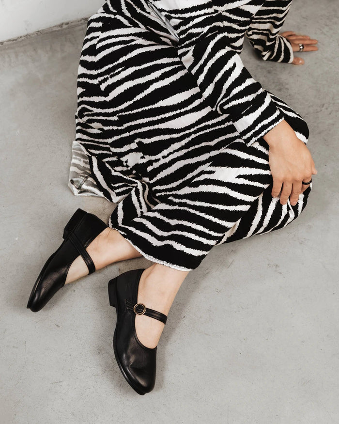 Side view of a leather Mary Jane flat with round toe and ankle strap. The Modern-Day Mary Jane Blackout. Sizes 5–12.