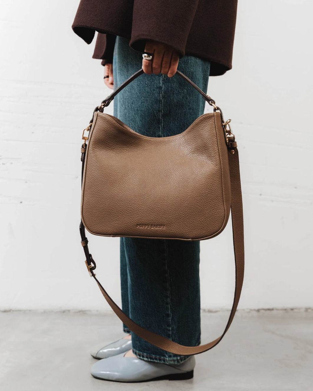 Woman wearing the leather hobo bag crossbody with ankle boots. The Sixteenth Tote Tapenade.