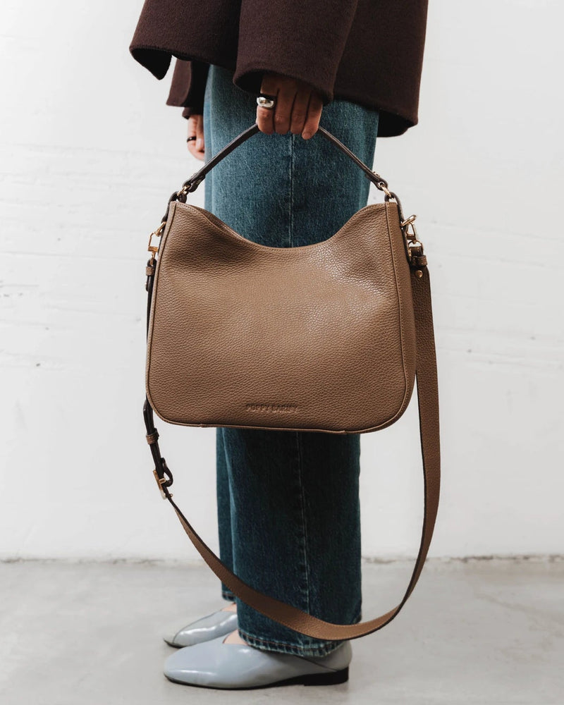 Woman wearing the leather hobo bag crossbody with ankle boots. The Sixteenth Tote Tapenade.