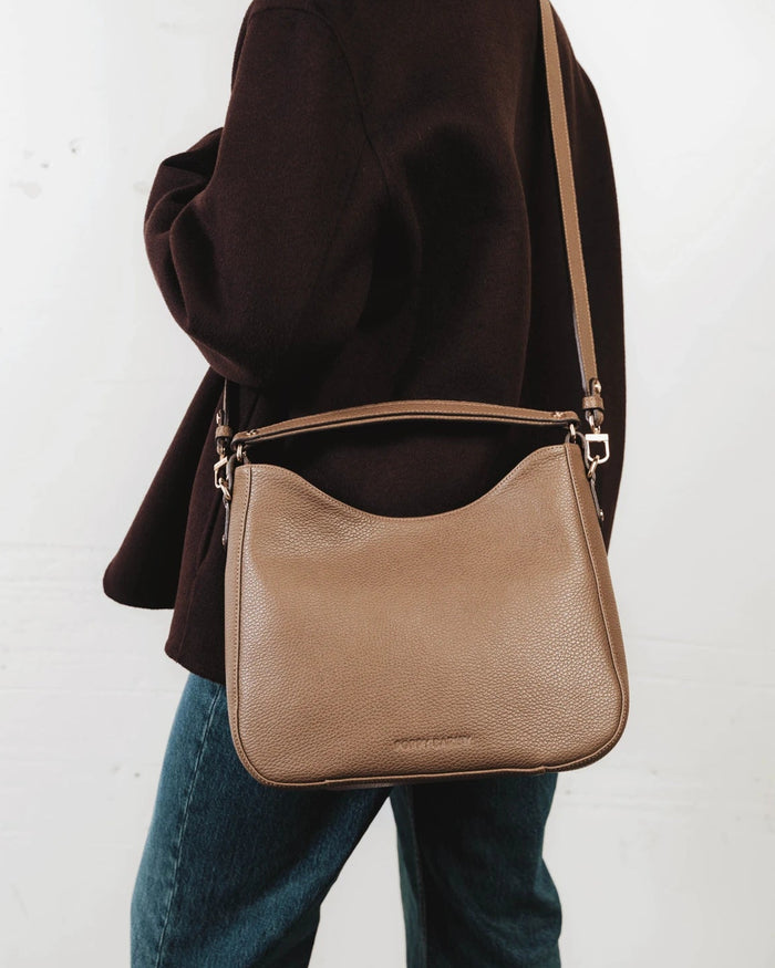Front view of the leather hobo bag with a long adjustable strap laid flat. The Sixteenth Tote Tapenade.