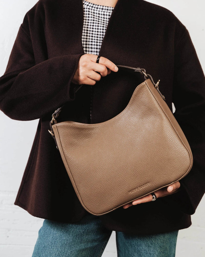 Woman holding the leather hobo bag in the crook of her arm. The Sixteenth Tote Tapenade.