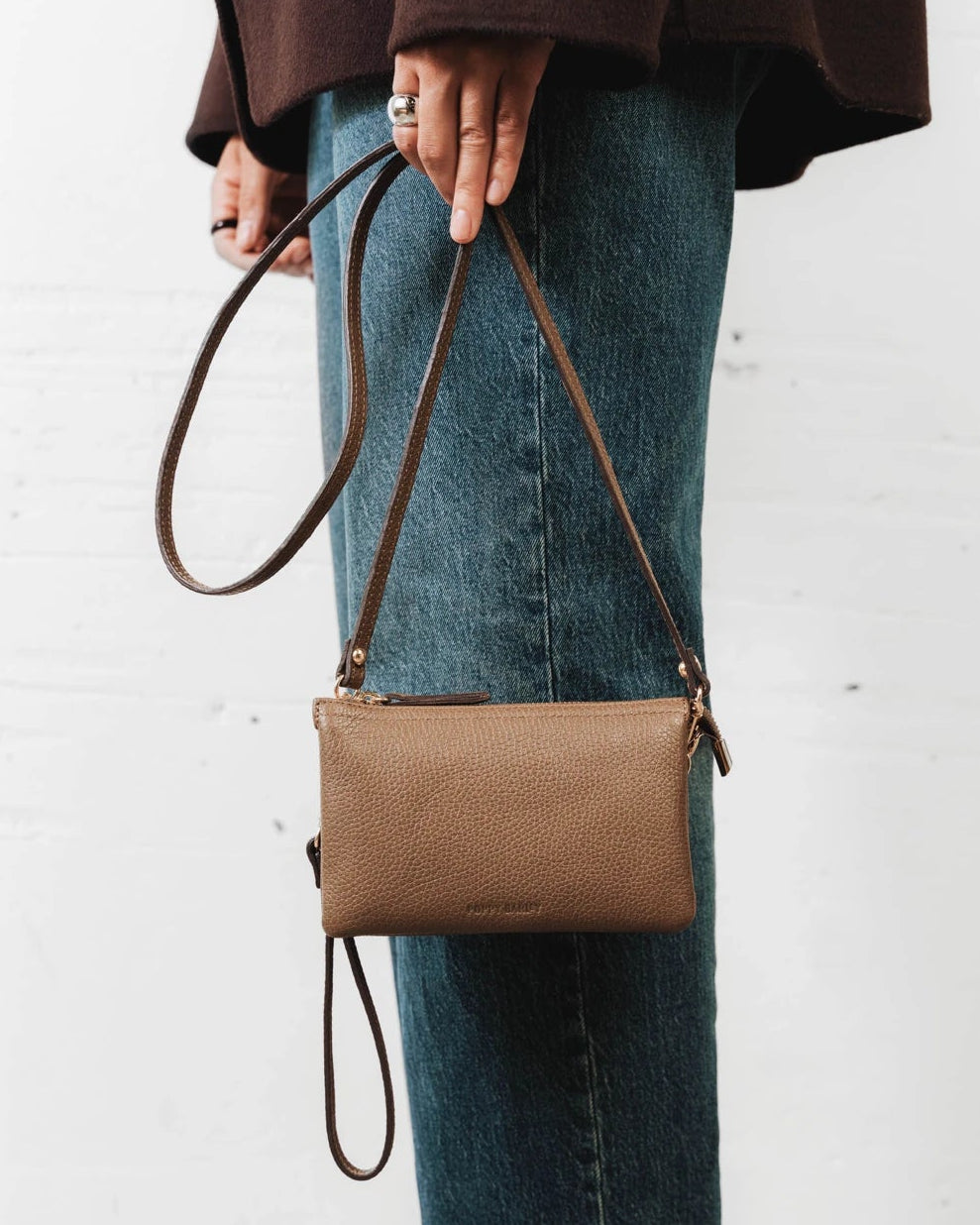 Woman wearing the pebbled-leather wristlet crossbody over jeans. The 3-in-1 Wristlet Tapenade.