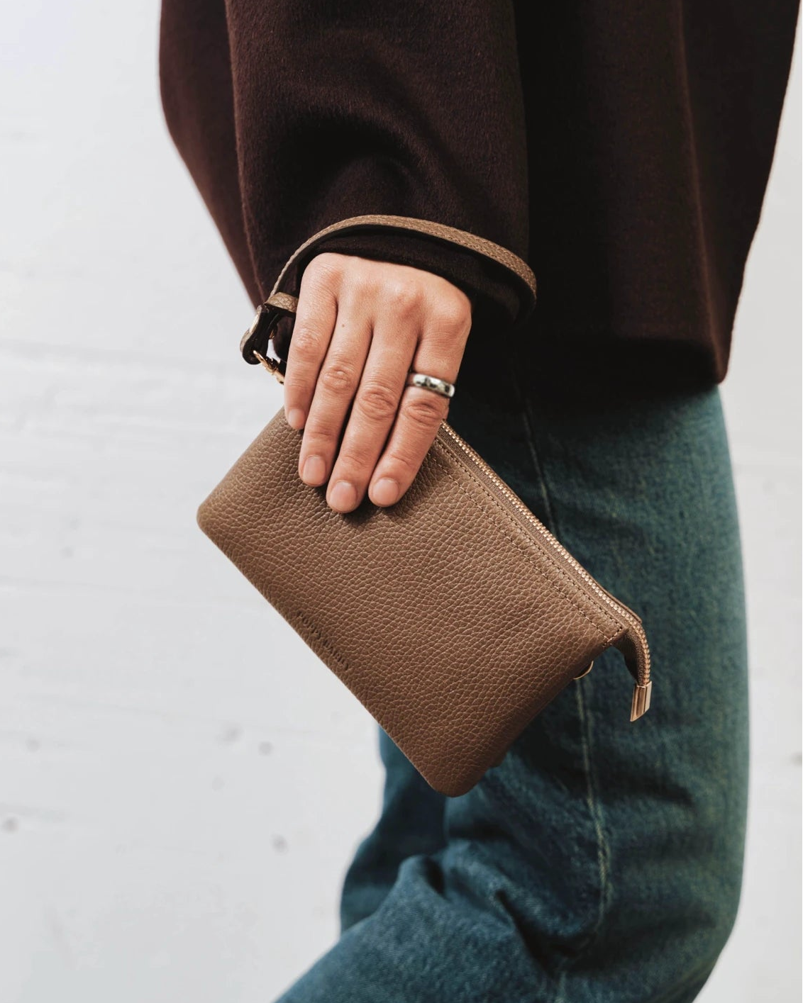 Woman holding the pebbled-leather wristlet by its wrist strap. The 3-in-1 Wristlet Tapenade.