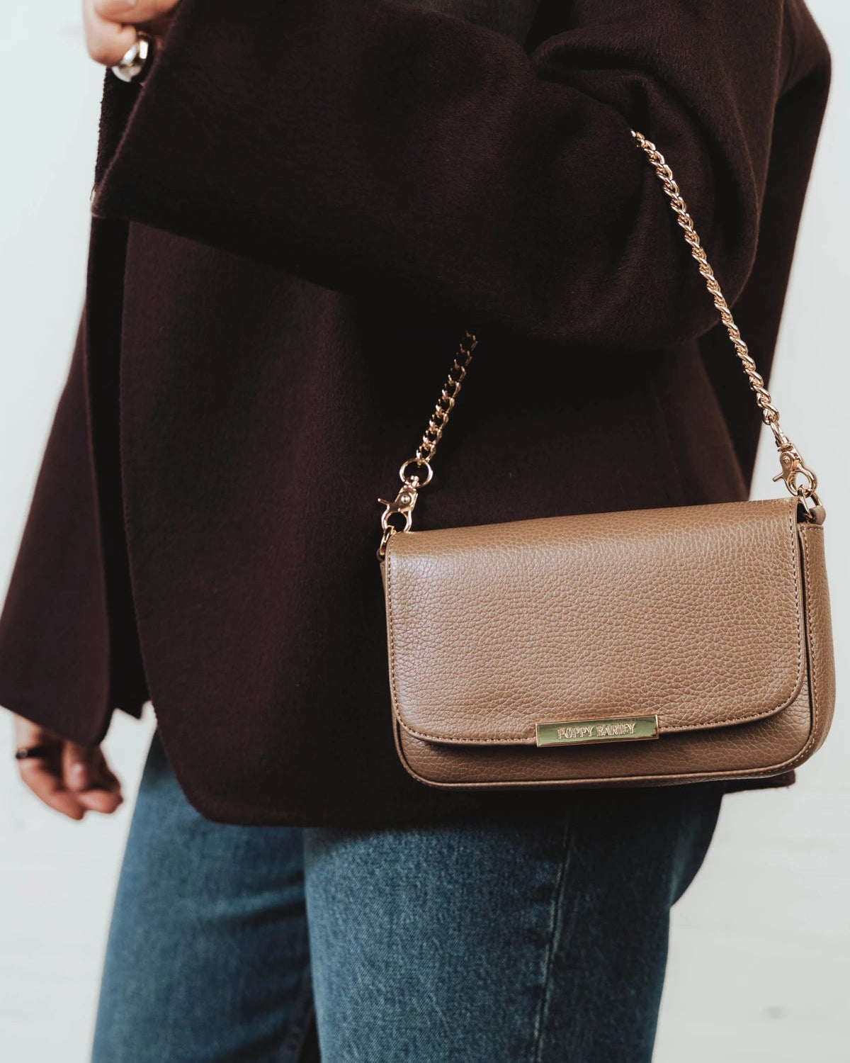 Woman wearing the leather flap bag over one shoulder. The Day To Night Bag Tapenade.