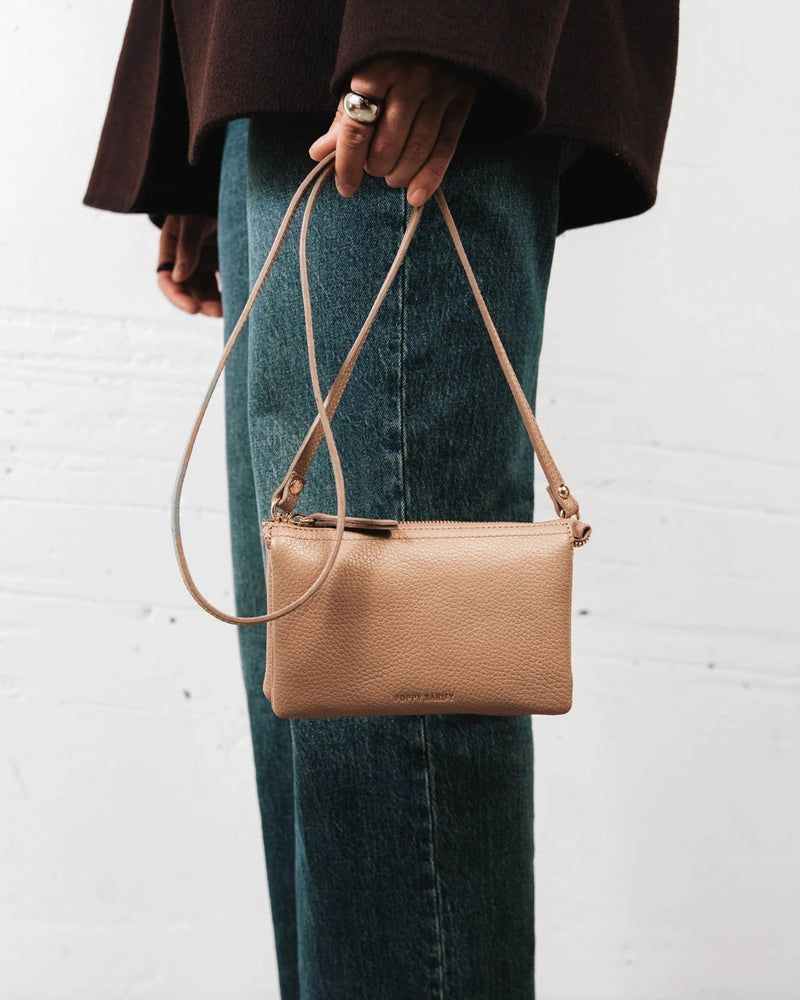 Woman wearing the pebbled-leather wristlet crossbody over jeans. The 3-in-1 Wristlet Biscotti Pebble.