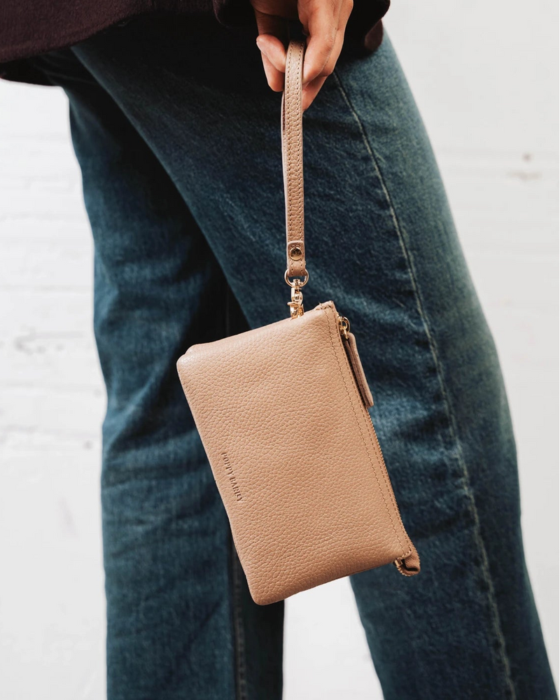 Woman holding the pebbled-leather wristlet by its wrist strap over jeans. The 3-in-1 Wristlet Biscotti Pebble.