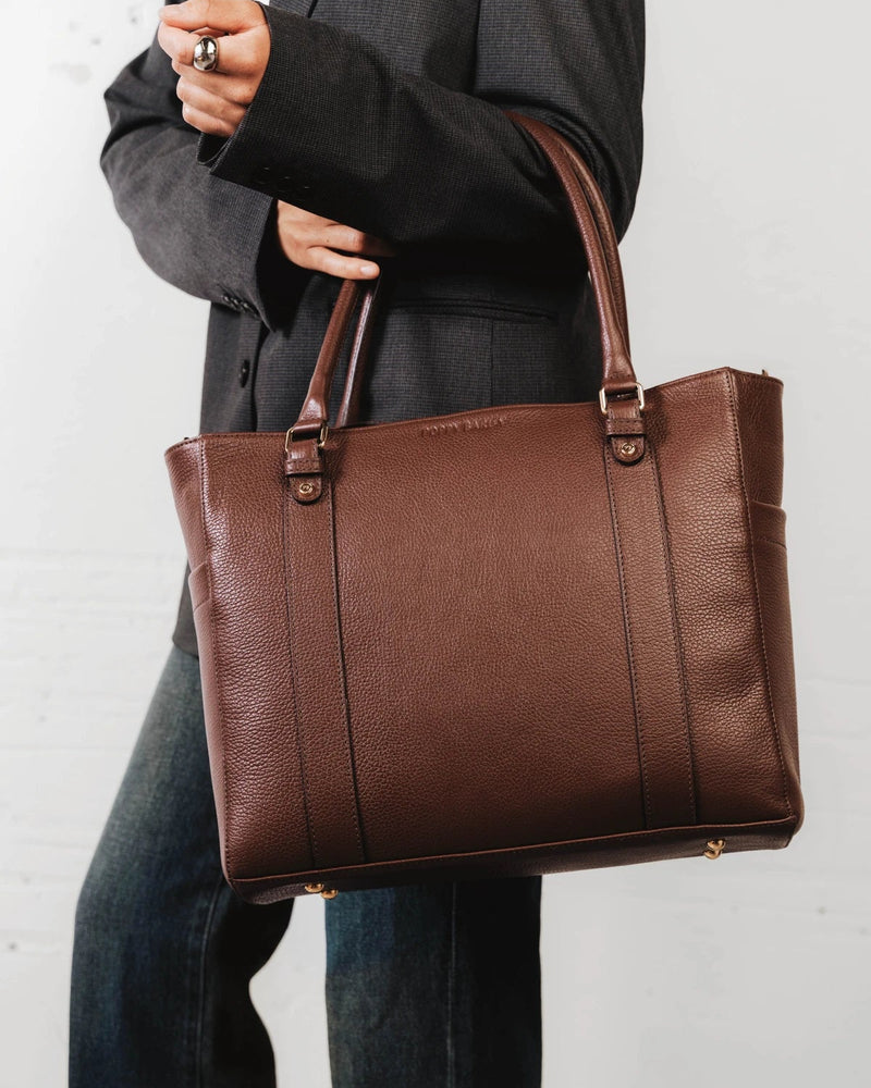 Woman carrying the leather tote by its top handles. The Colleague Tote French Press.