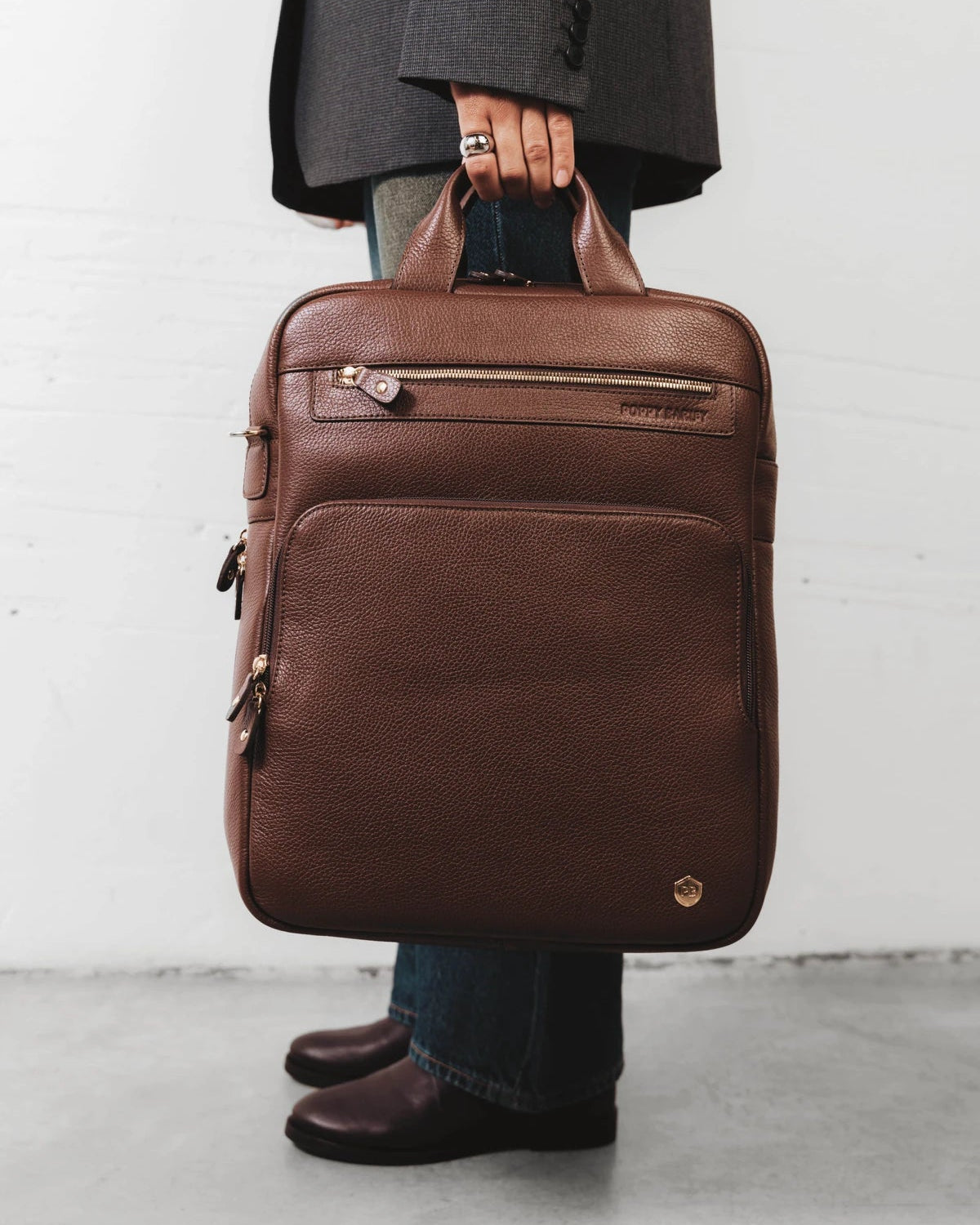 Person carrying the pebbled-leather backpack by its top handle. The Backpack French Press.
