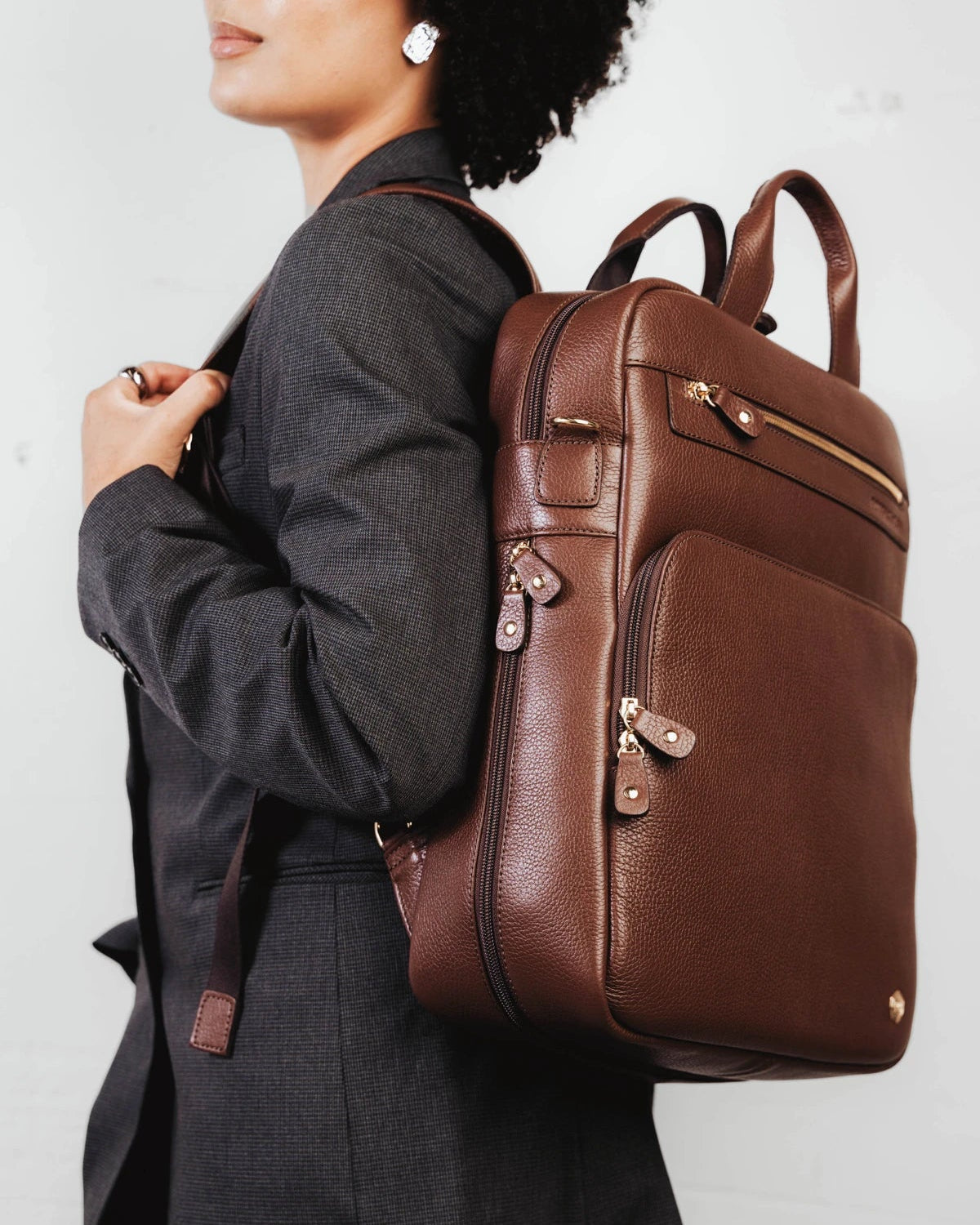 Woman wearing the pebbled-leather backpack over one shoulder. The Backpack French Press.