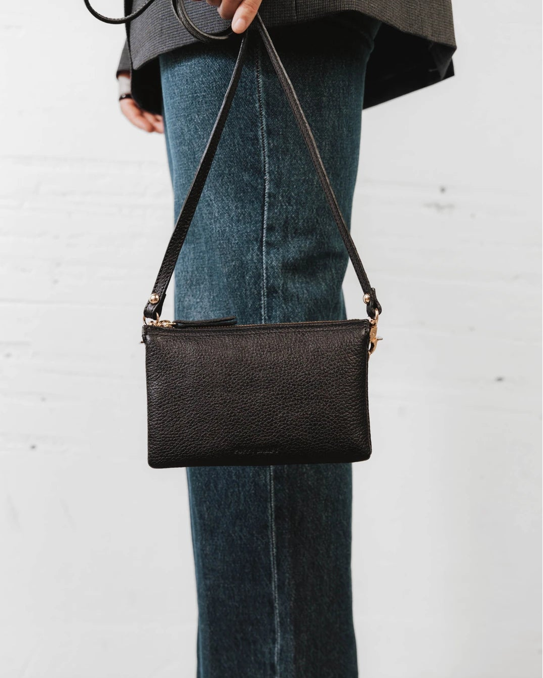 Woman wearing the pebbled-leather wristlet crossbody over jeans. The 3-in-1 Wristlet Black.