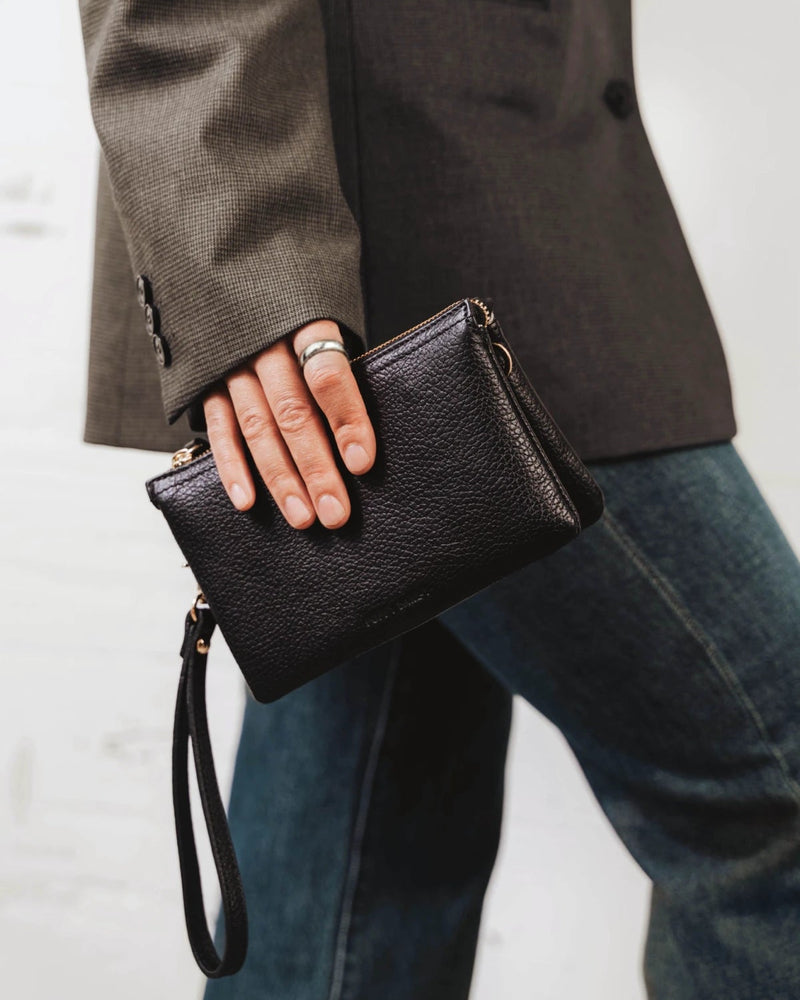 Woman holding the pebbled-leather wristlet by its strap. The 3-in-1 Wristlet Black.